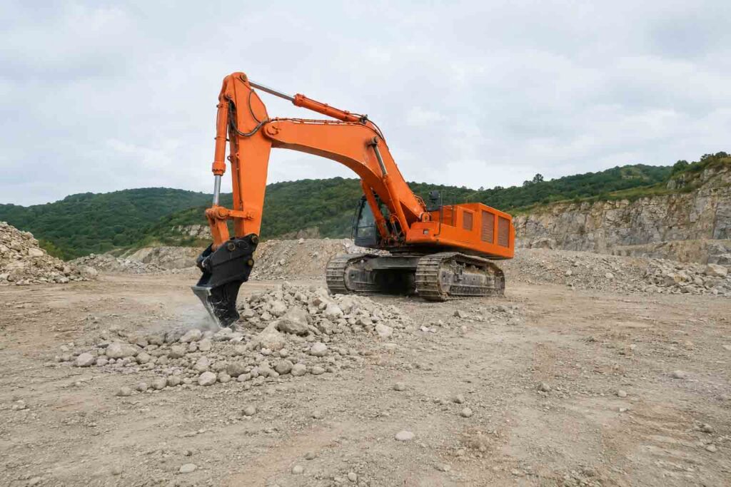 Excavator ripper attachment working on roots, stumps, or compacted ground before bucket removal